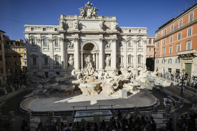 Tourists toss coins over a makeshift pool as Rome’s Trevi Fountain undergoes maintenance